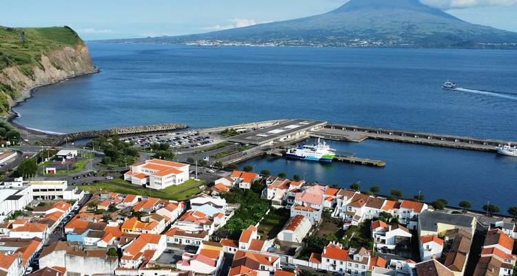 Kustplaats met oranje daken en veerhaven omlijst door diepblauwe Atlantische wateren en de vulkanische kegel van Mount Pico aan de overkant van het kanaal.