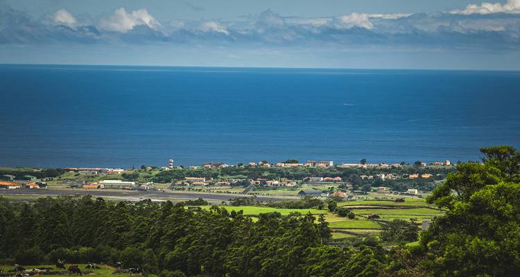 High vantage of green farmlands, airport runway and a coastal village meeting the vast blue Atlantic horizon.