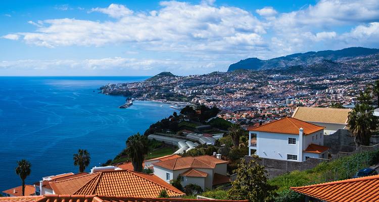 Large panorama côtier sur la ville de Funchal étalée le long du littoral accidenté de Madère et de l'Atlantique bleu profond.