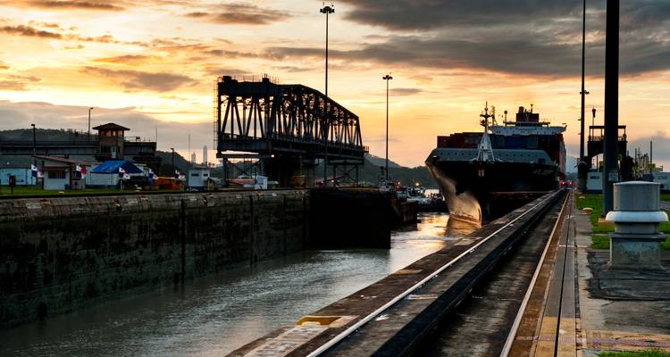 Frachtschiff fährt in eine Kanalschleuse bei Sonnenuntergang mit dramatischem orangefarbenem Himmel und Silhouetten ein