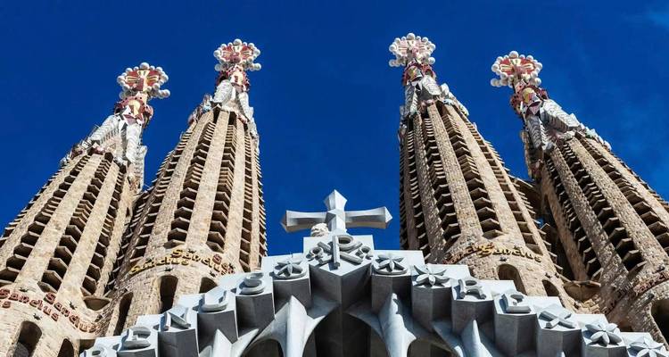 Vista hacia arriba de cuatro agujas ornamentadas de la Sagrada Familia contra un cielo azul profundo