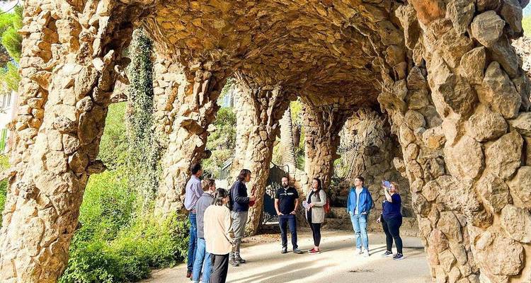 Grupo de turistas escuchando bajo las columnatas de piedra de los viaductos del Parque Güell rodeados de roca natural