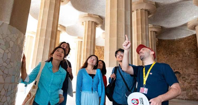 Guía explicando la arquitectura de Gaudí a un pequeño grupo de turistas bajo columnas altas en el Park Güell