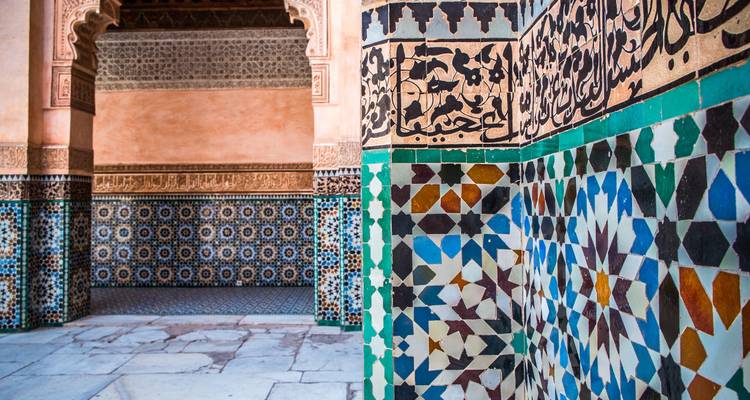 Ingewikkelde zellij mozaïektegels en gesneden pleisterwerk in een historische Marokkaanse madrasa.
