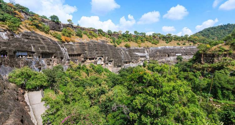 Weelderige beboste kloof met een rij in de rots uitgehouwen Ajanta-grotingangen langs een grijze klif.
