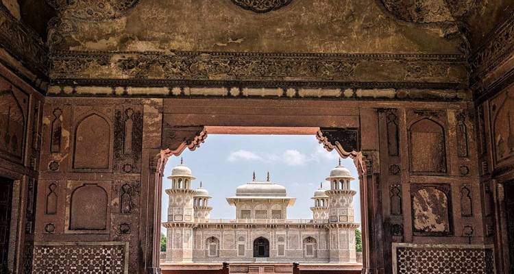 Elegant Mughal mausoleum omlijst door een sierlijke boog binnen het Agra Fort complex.