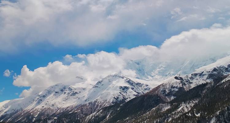 Amplias montañas nevadas con nubes flotando sobre los picos contra un cielo azul