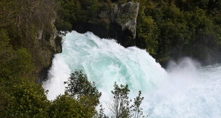 Turbulent turquoise water dat over Huka Falls stroomt, omringd door weelderige vegetatie.