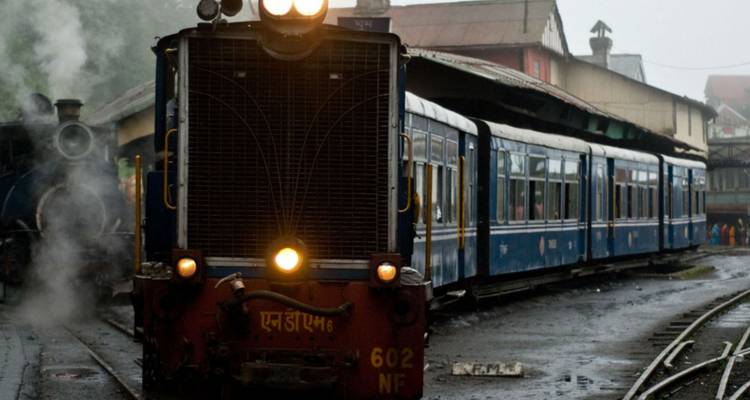 Blauwe smalspoortrein met koplamp stoomt op station Darjeeling op een mistige ochtend.