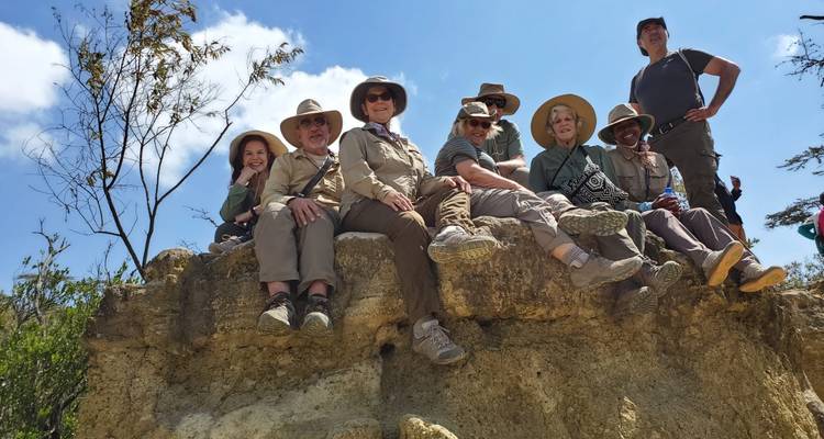 Grupo de excursionistas sentados en la cima de un afloramiento rocoso bajo un cielo azul brillante.