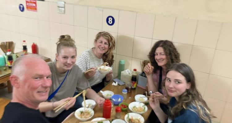 Des amis savourent des bols fumants de nouilles dans un petit restaurant local simple, souriant pour une photo rapide.