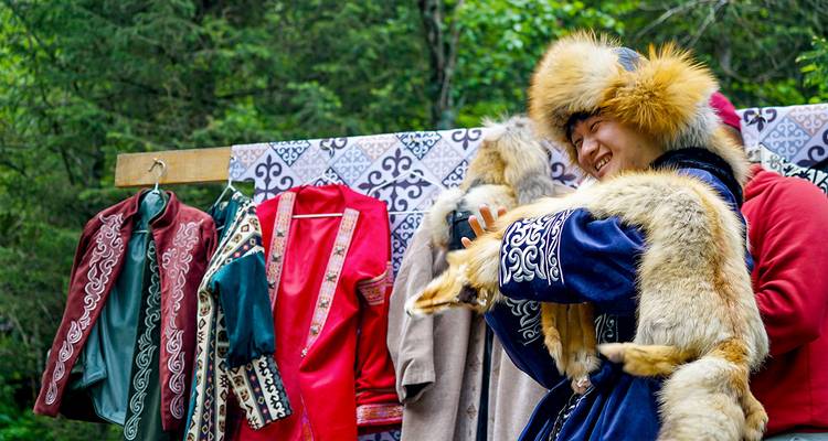 Glimlachende vrouw past een traditionele bontmuts en vossenvacht aan bij een openlucht kostuumkraam