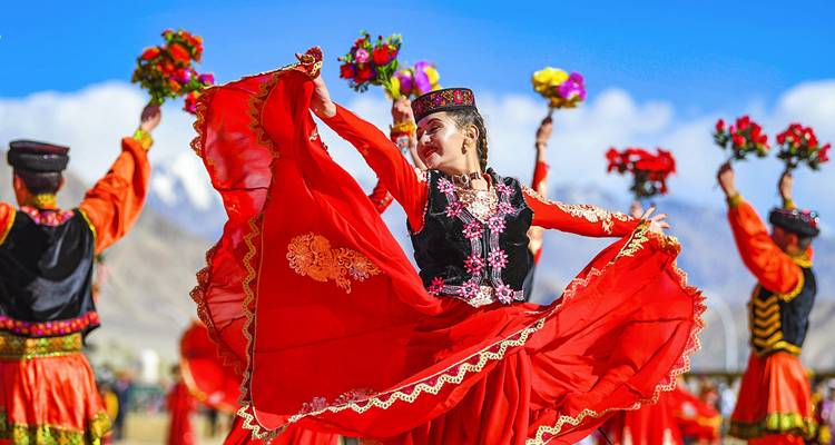 Levendige volksdansers in rode kostuums draaien met bloemen tegen een bergachtergrond