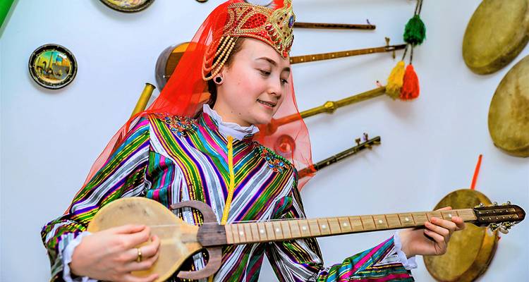 Jonge muzikant in kleurrijk gestreept kostuum bespeelt een traditioneel snaarinstrument binnenshuis