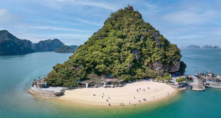 Luftaufnahme der Insel Titov mit halbmondförmigem Weißstrand und türkisfarbenem Wasser, das mit Besuchern übersät ist.