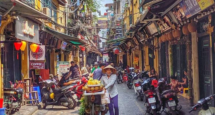 Enge Straße im Alten Viertel von Hanoi, belebt mit Motorrädern, Stromleitungen über Kopf und kleinen Geschäften auf beiden Seiten.