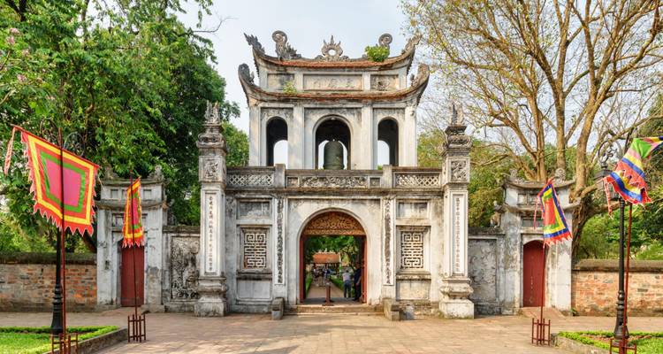 Historisches Tor des Tempels der Literatur von Hanoi, umrahmt von Bäumen und farbenfrohen Bannern.