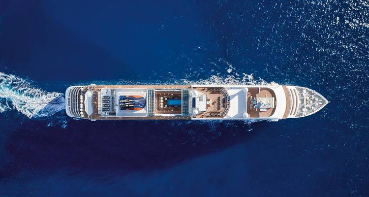 Drohnenaufnahme von oben auf ein großes Kreuzfahrtschiff, das durch tiefblaues Meer fährt.