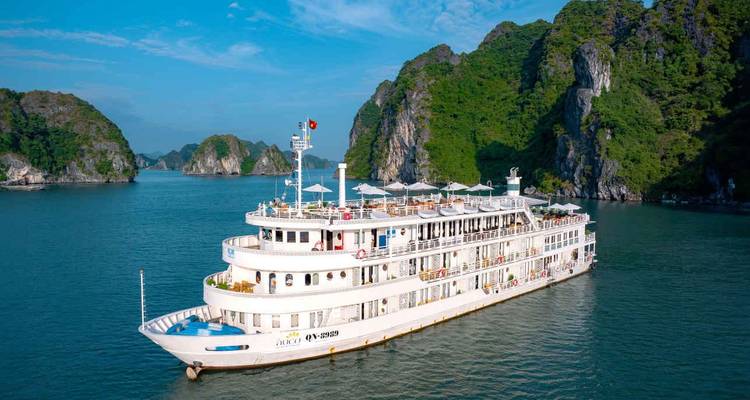 Weißes mehrstöckiges Kreuzfahrtschiff, das zwischen dramatischen Kalksteininseln in der Halong-Bucht segelt.