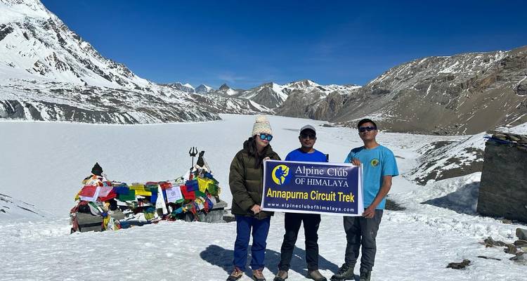 Tres excursionistas posan con una pancarta del Circuito de Annapurna en un paso de alta montaña nevado
