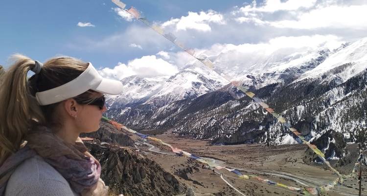 Una excursionista contempla un amplio valle del Himalaya con banderas de oración ondeando