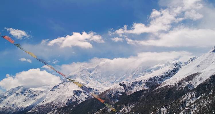 Picos cubiertos de nieve detrás de una hilera de banderas de oración coloridas bajo un cielo brillante