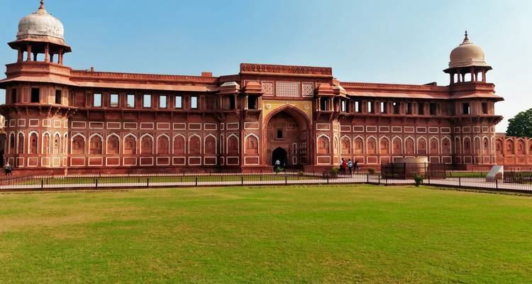 Les murs de grès rouge et les tours à coupole du Fort d'Agra s'élèvent au-dessus de pelouses vertes bien entretenues sous un ciel dégagé.