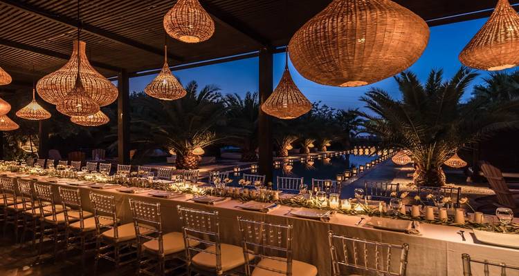 Eleganter langer Esstisch neben beleuchtetem Pool mit geflochtenen Laternen bei Nacht.