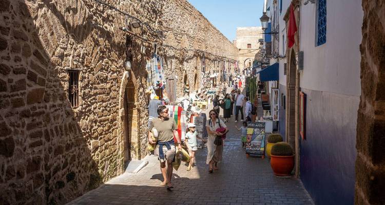 Belebte enge Straße in Essaouiras Medina mit Einkäufern und Steinmauern.
