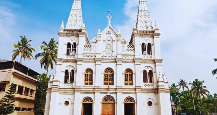 Weiße neugotische Kirche mit Zwillingstürmen, eingerahmt von Palmen unter hellem Himmel