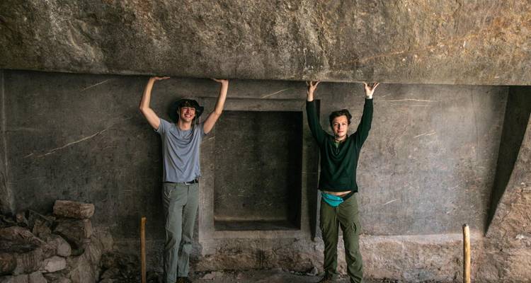 Twee wandelaars die doen alsof ze een massieve stenen plaat omhoog houden binnen een oude structuur.