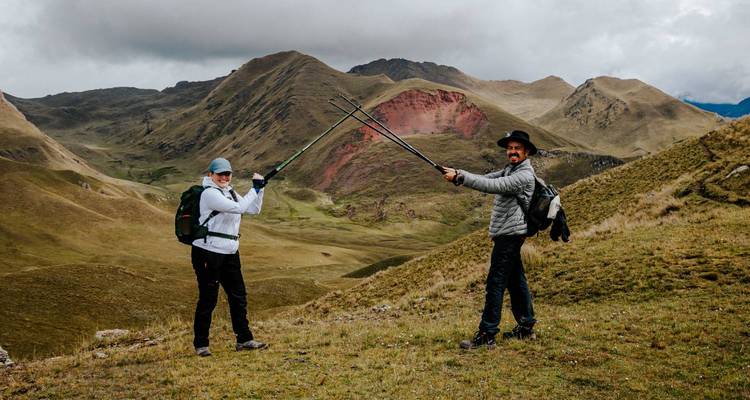 Twee trekkers raken trekkingstokken aan in een groene bergvallei onder bewolkte luchten.