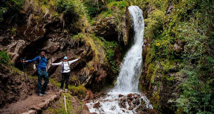 Wandelaars vieren voor een waterval langs een bospad.