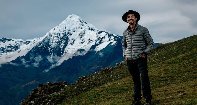 Reiziger staat glimlachend voor een met sneeuw bedekte Andesberg onder bewolkte luchten.