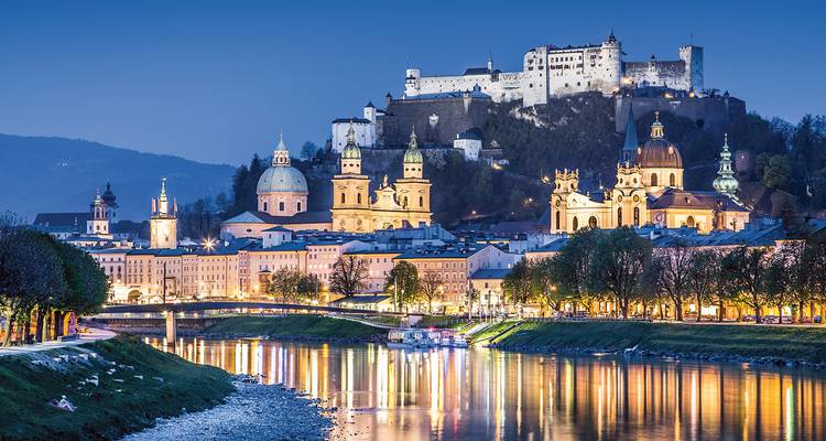 Vue à l'heure bleue de la vieille ville de Salzbourg avec la forteresse illuminée se reflétant dans la rivière.
