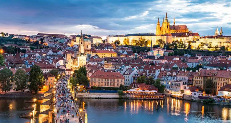 Vue crépusculaire sur le pont Charles bondé de visiteurs et le château de Prague illuminé au-dessus de la rivière Vltava.