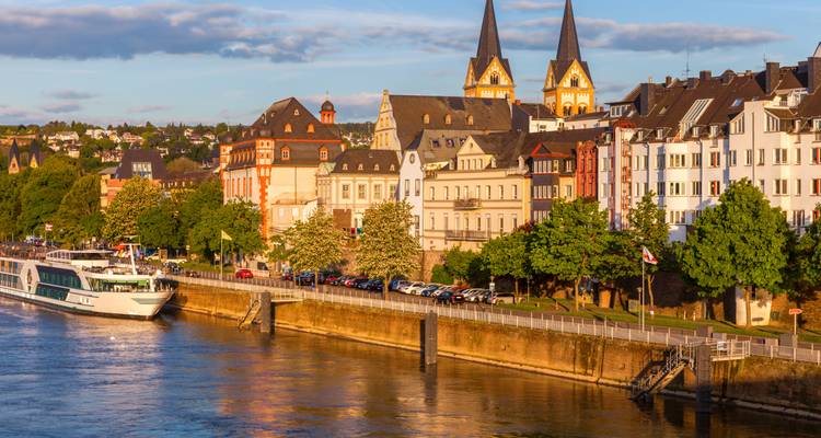 La lumière dorée du soir illumine les façades riveraines et les clochers d'une ville historique allemande avec un bateau de croisière sur le Rhin.