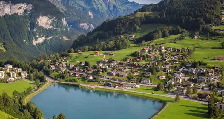 Village suisse alpin avec des chalets autour d'un lac turquoise adossé à des montagnes vertes.