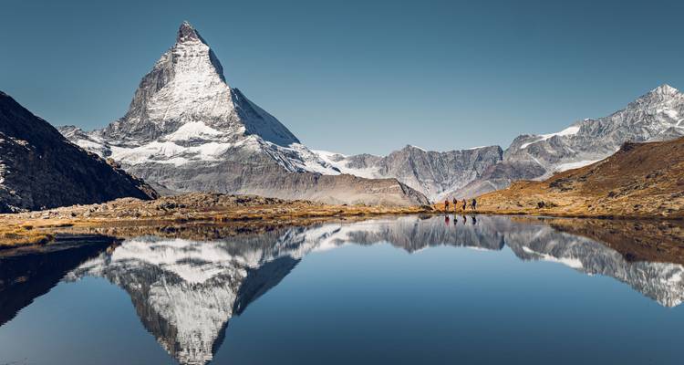 Reflet parfait du Cervin et des sommets enneigés dans un lac alpin immobile sous un ciel dégagé.