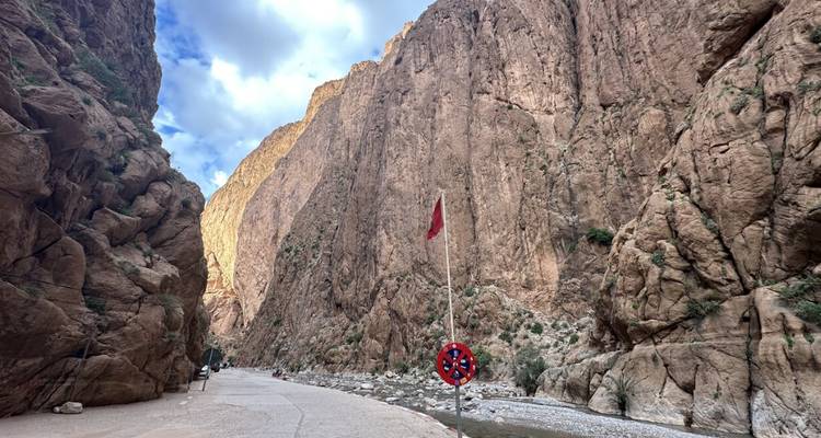 Enge Canyonstraße mit marokkanischer Flagge, umgeben von hoch aufragenden Felswänden.