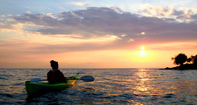 Un kayakiste solitaire observe un coucher de soleil orange vibrant se refléter sur les eaux tranquilles du lac.