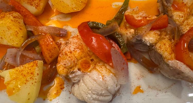 Bord met gebakken vis, paprika's en aardappelen bedekt met een levendige paprikakleurige saus