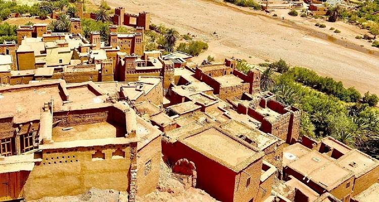 Luchtfoto van adobe versterkte kasbah-gebouwen naast een droge rivierbed en palmen