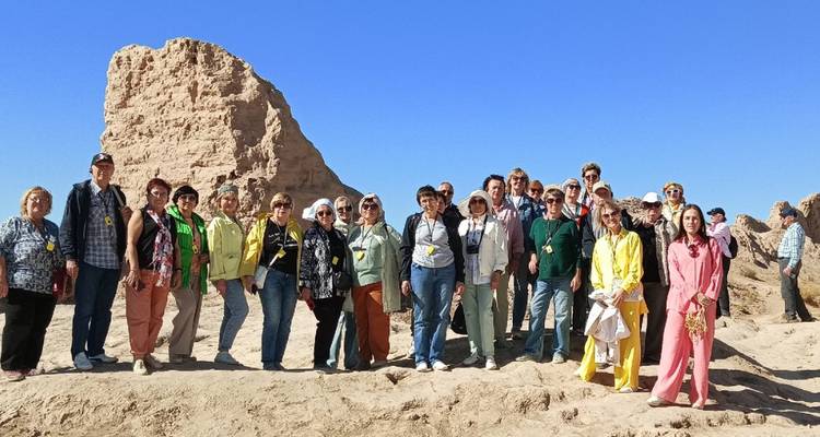Een grote toeristische groep poseert op een rotsachtige woestijnuitloper met een heldere blauwe lucht erboven.