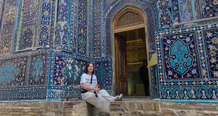 Reiziger zit op betegelde treden naast een sierlijke blauwe gemusterde mausoleum deuropening.