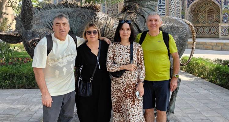 Vier reizigers staan glimlachend voor een bronzen dierensculptuur en een betegelde madrasa-gevel.