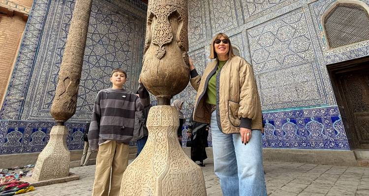 Vrouw en jongen verkennen een binnenplaats met hoge gebeeldhouwde stenen zuilen en ingewikkeld blauw tegelwerk.