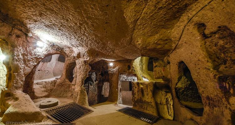 Pasajes iluminados de una ciudad subterránea tallada en roca blanda con suelos enrejados y lámparas.