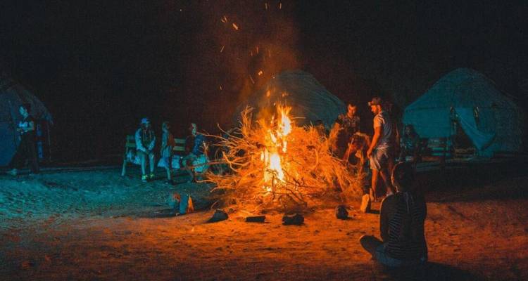 Kampeerders zitten rond een laaiiend kampvuur in de woestijnnacht naast joerttenten.
