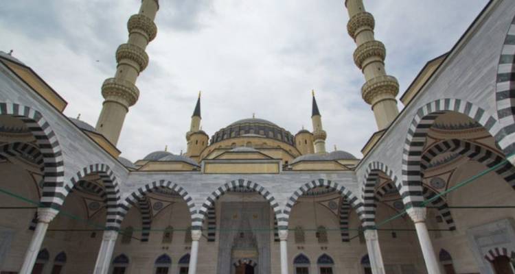 Binnenplaats van een grote moskee in Ottomaanse stijl met gestreepte bogen en meerdere minaretten gezien van onderaf.